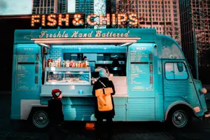 Blue Fish & Chips Food Truck with a woman carrying a backpack and a little boy