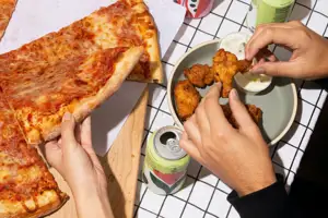 Hands Serving Up Pizza And Wings With A Couple Soda Cans In The Picture As Well