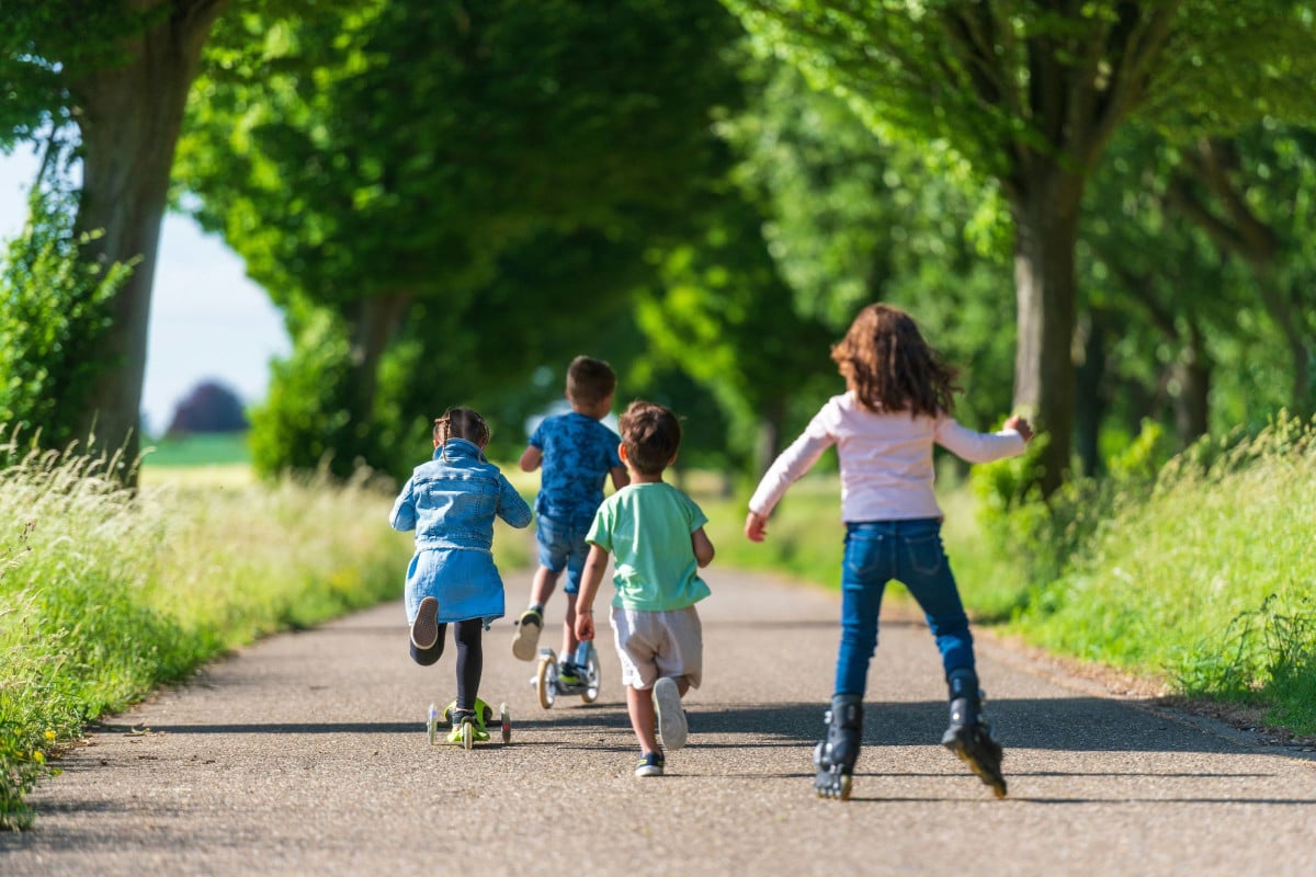 4 kids are playing on scooters and roller blades on a path